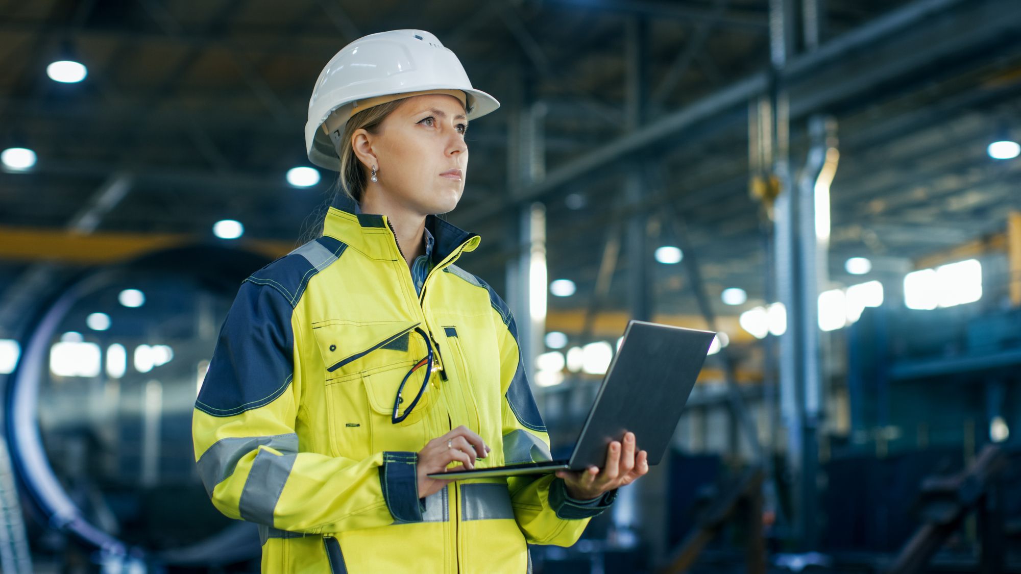 woman with hardhat holding a laptop in a warehouse